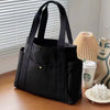 Bolso tote de lona negra con tirantes apoyado sobre una superficie de madera junto a una planta en maceta.