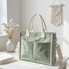 Sac cabas vert clair en velours côtelé avec une sangle en toile naturelle, exposé sur une surface en bois blanc.