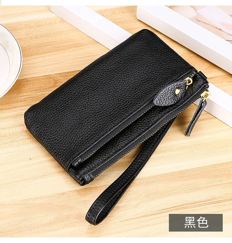Black genuine leather wristlet clutch wallet with zipper closure resting on a wooden surface.