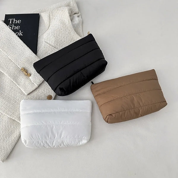 A collection of quilted cosmetic travel bags in black, tan, and white resting on a white surface.