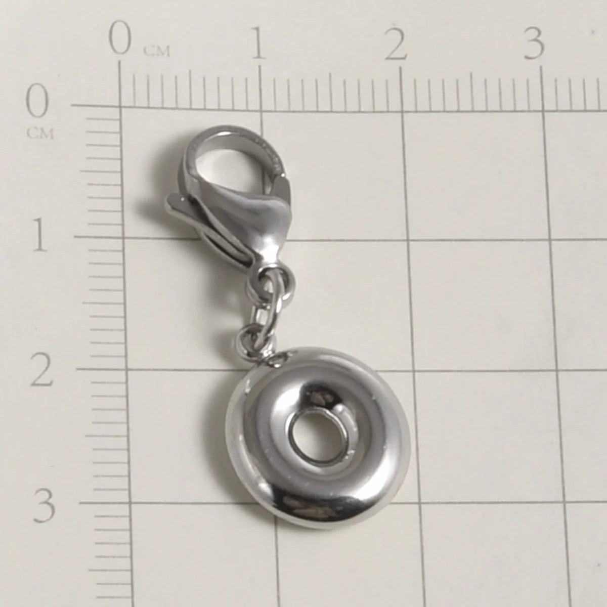 Silver stainless steel alphabet letter charm with a lobster clasp placed on a ruler.