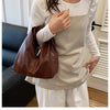 A woman wearing a white top and light apron holds a brown leather crossbody tote bag.
