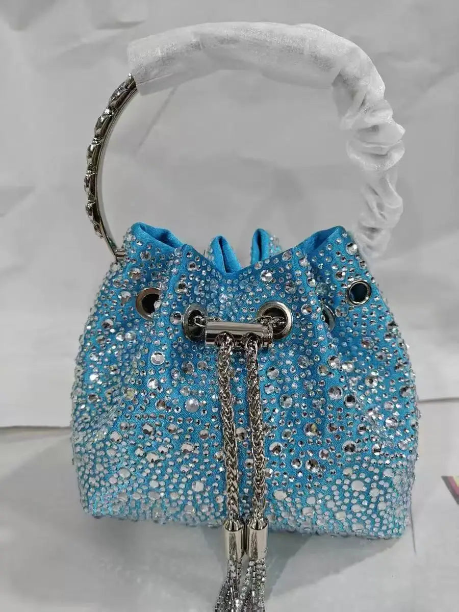 A bright blue crystal-embellished evening clutch with a silver chain strap is displayed against a white background.