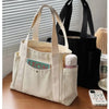 Una bolsa de lona beige con bolsillo y un termo blanco, junto a una bolsa de lona negra, sobre una superficie de madera.