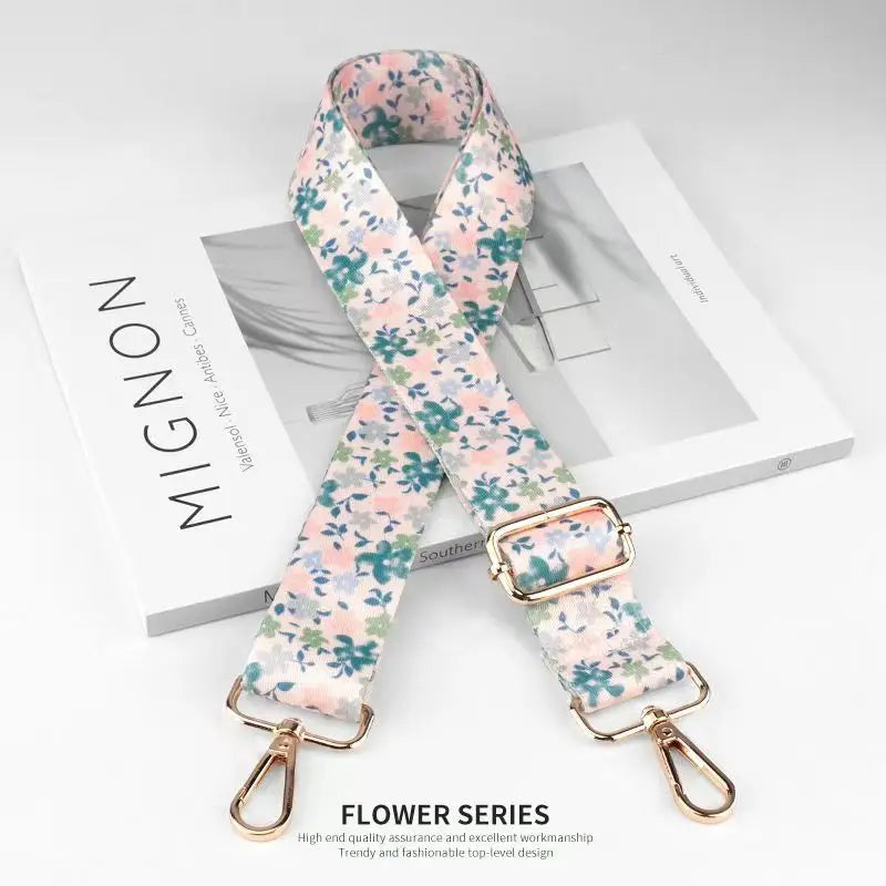 A pink floral patterned nylon bag strap with a gold buckle is displayed on a white box.