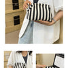 A woman holds a black and white striped summer crochet handbag in a light-colored shirt.