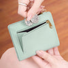 A hand is holding a light mint green minimalist RFID blocking wallet with a gold clasp and a silver card.