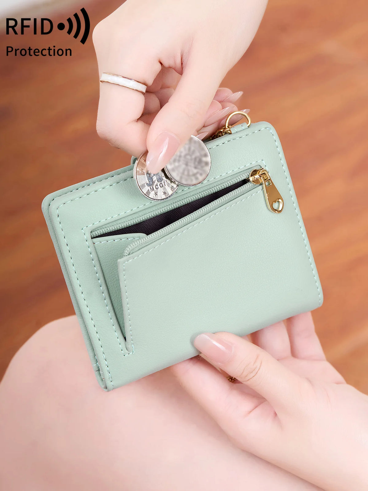 A hand is holding a light mint green minimalist RFID blocking wallet with a gold clasp and a silver card.