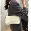A woman holds a cream-colored vintage curved flap shoulder bag against her dark gray coat.