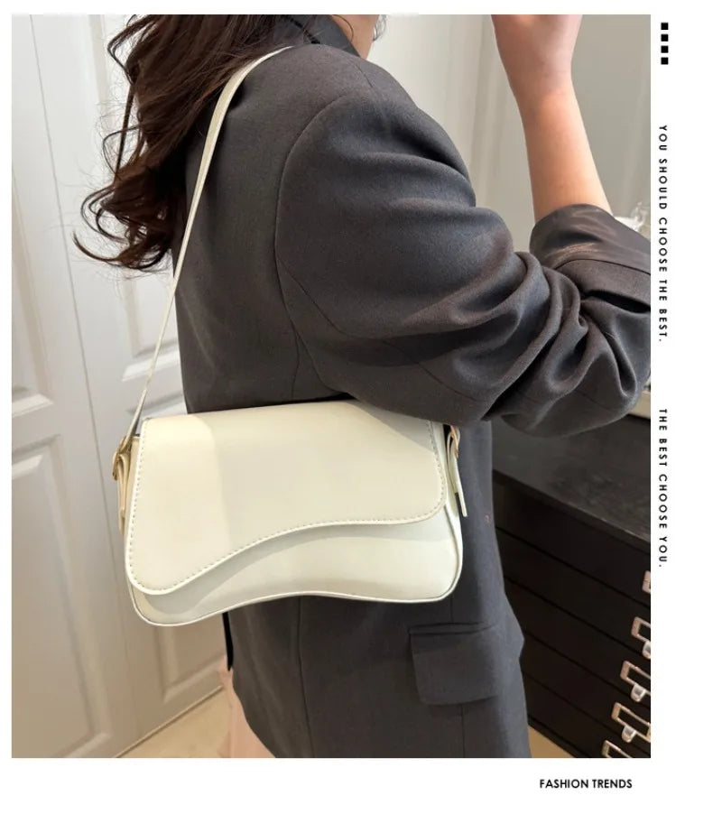A woman holds a cream-colored vintage curved flap shoulder bag against her dark gray coat.