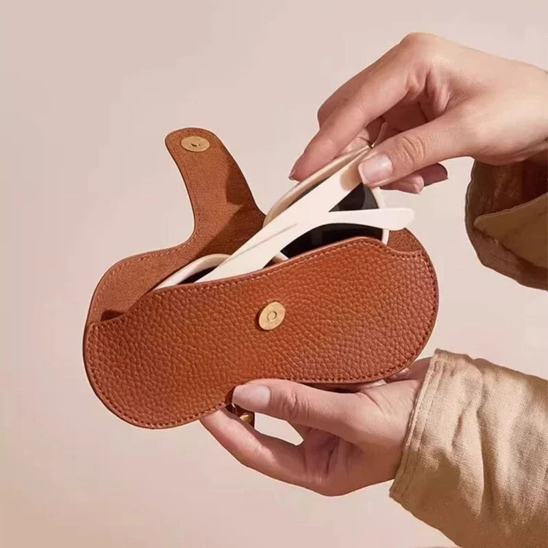 Una mano está colocando una correa de cuero blanco en una funda para gafas de sol de cuero marrón delgado.
