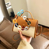 A hand holds a tan leather handbag with a multi-color acrylic chain strap against a neutral background.