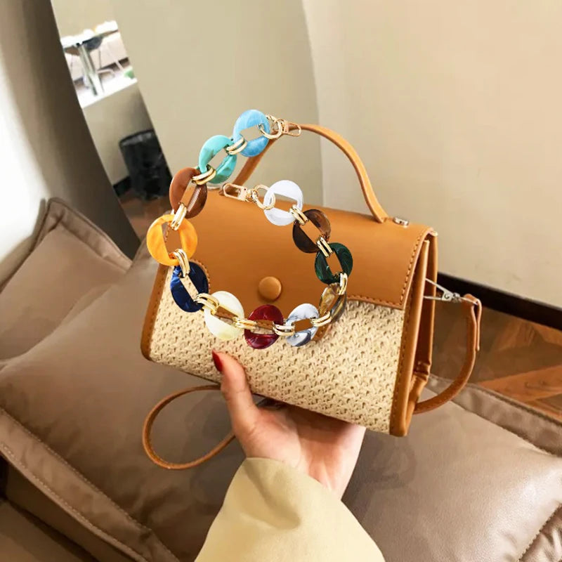 A hand holds a tan leather handbag with a multi-color acrylic chain strap against a neutral background.