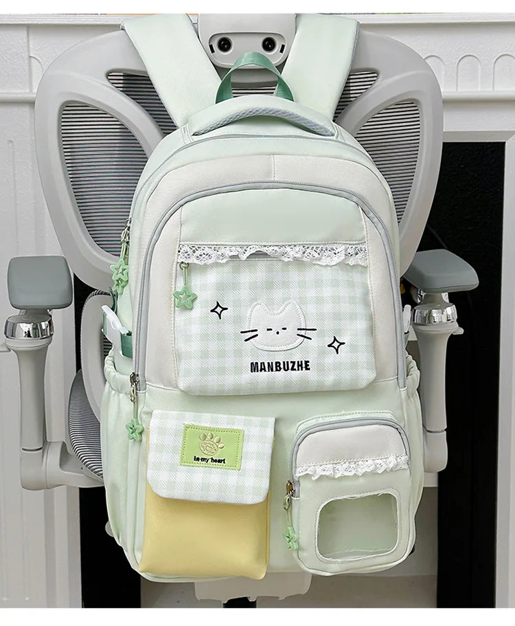 A light green backpack with a cat design and lace trim hanging on a white coat rack.