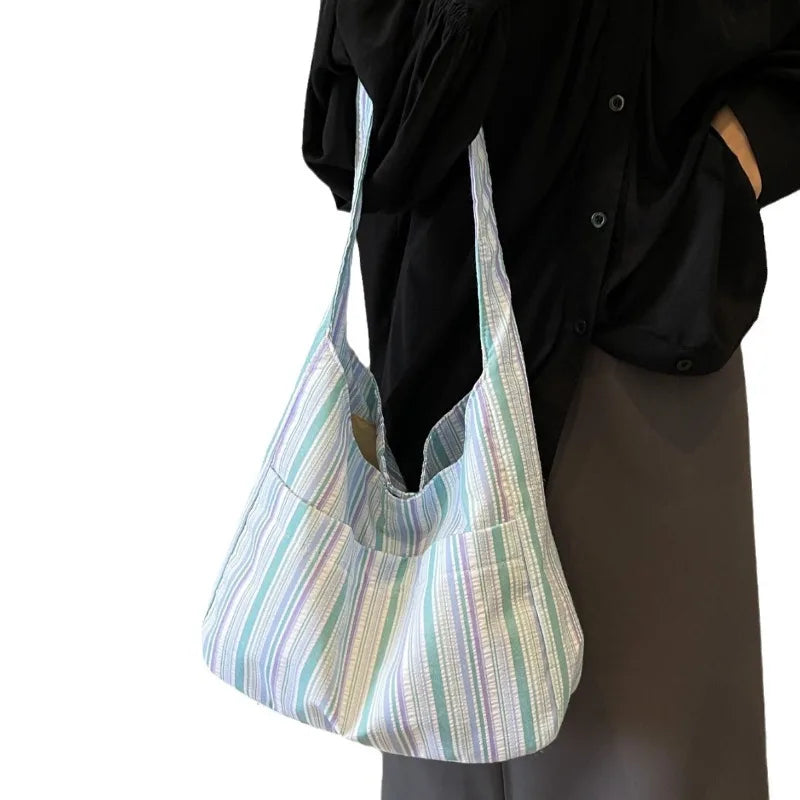 A light striped canvas shoulder bag hanging from a black shirt.