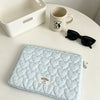 A light blue quilted laptop sleeve with a pattern of small hearts is displayed on a white table next to a mug and sunglasses.
