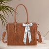 A brown PU leather laptop tote bag with a white floral scarf tied as a bow, displayed on a light surface.