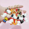 A hand holds a set of Snoopy 3D silicone keychains featuring various styles and colors.