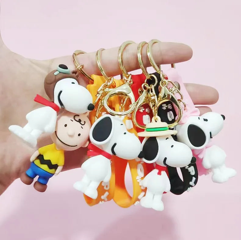 A hand holds a set of Snoopy 3D silicone keychains featuring various styles and colors.