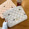A light blue quilted laptop sleeve with black tie-shaped embroidery is shown next to a pink quilted fabric and a glass jar.