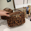 A brown leopard print faux suede cosmetic bag with a gold zipper is displayed on a white surface.