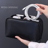 A hand is holding a black leather multi-layer cable organizer pouch with a wide opening, showing coiled white cables inside.