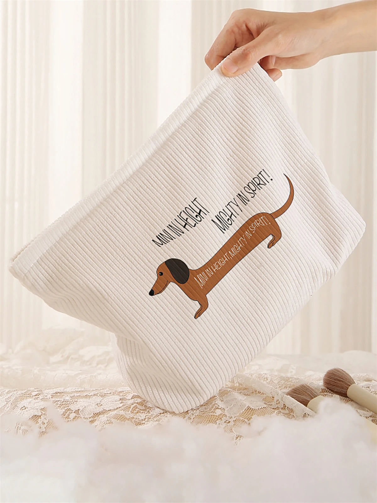 A beige corduroy makeup storage bag featuring a brown dachshund silhouette with text on it.