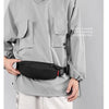 A person wearing a gray hooded jacket is holding a black messenger bag.