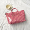 A pink striped transparent PVC tote bag is shown on a white surface next to a ceramic cup.