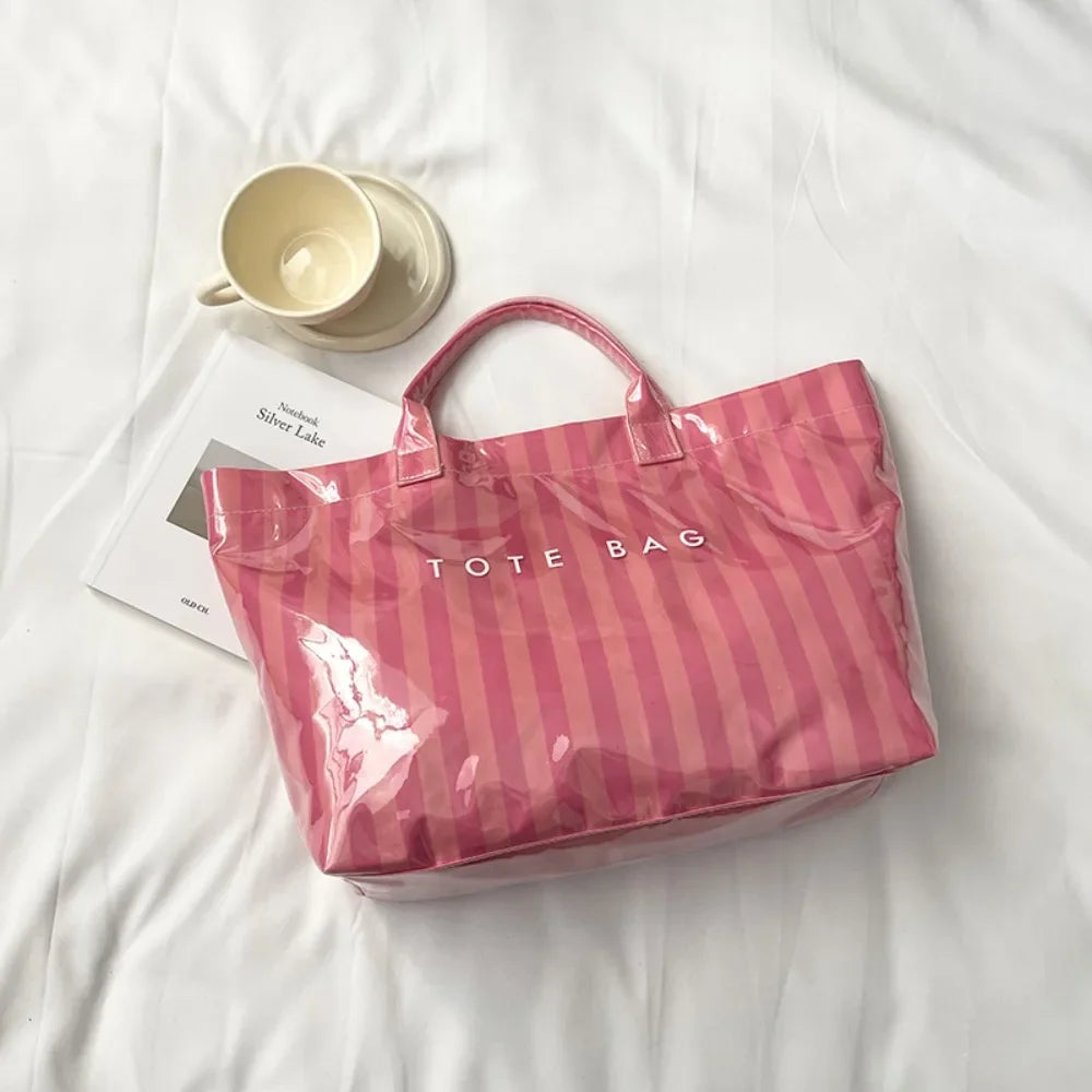 A pink striped transparent PVC tote bag is shown on a white surface next to a ceramic cup.