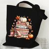 Black canvas tote bag featuring a print of a stack of books, an autumn pumpkin, and fall foliage.