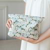 A woman holds a light blue floral canvas makeup bag with white and green flowers.