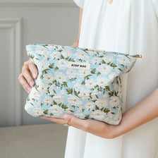 A woman holds a light blue floral canvas makeup bag with white and green flowers.