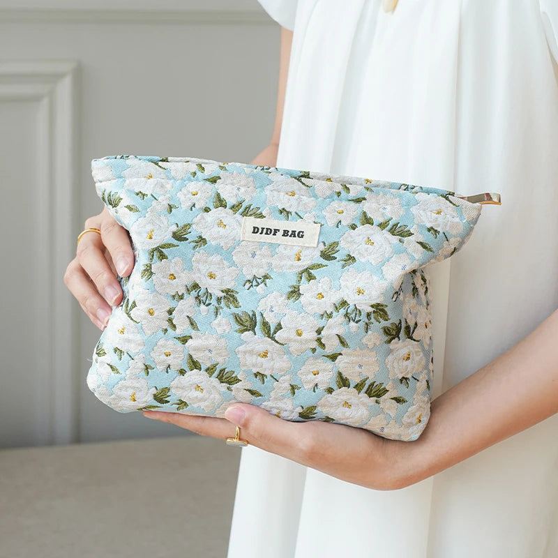 A woman holds a light blue floral canvas makeup bag with white and green flowers.