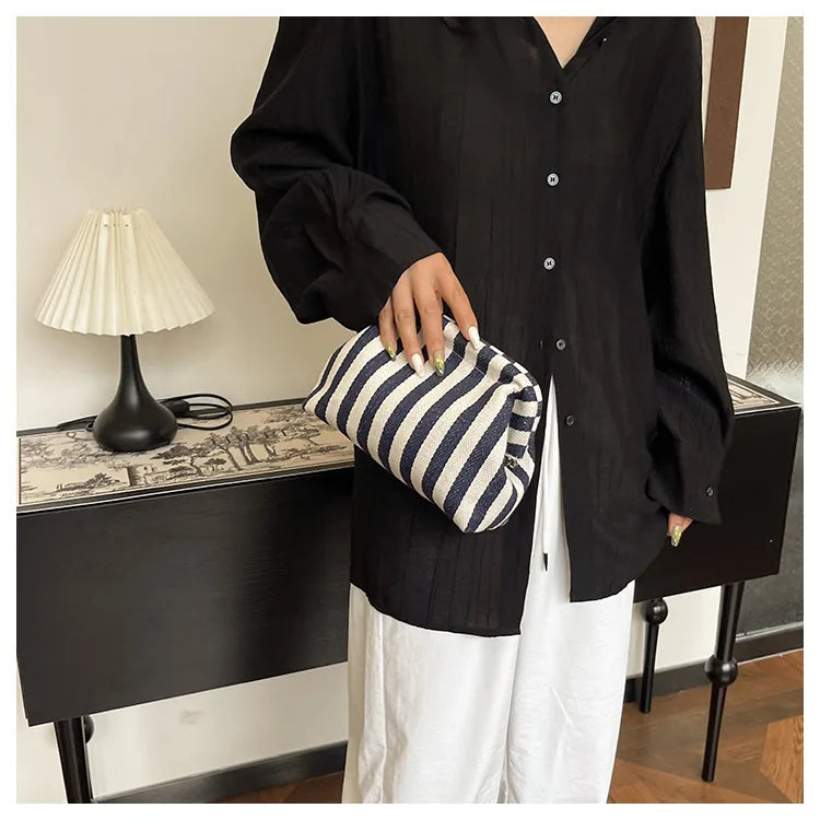 A woman holds a striped black and white crochet handbag while wearing a black shirt and white pants.