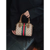 A brown leather tote diaper bag with a green and red striped pattern is held by a person.