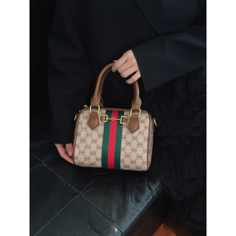 A brown leather tote diaper bag with a green and red striped pattern is held by a person.