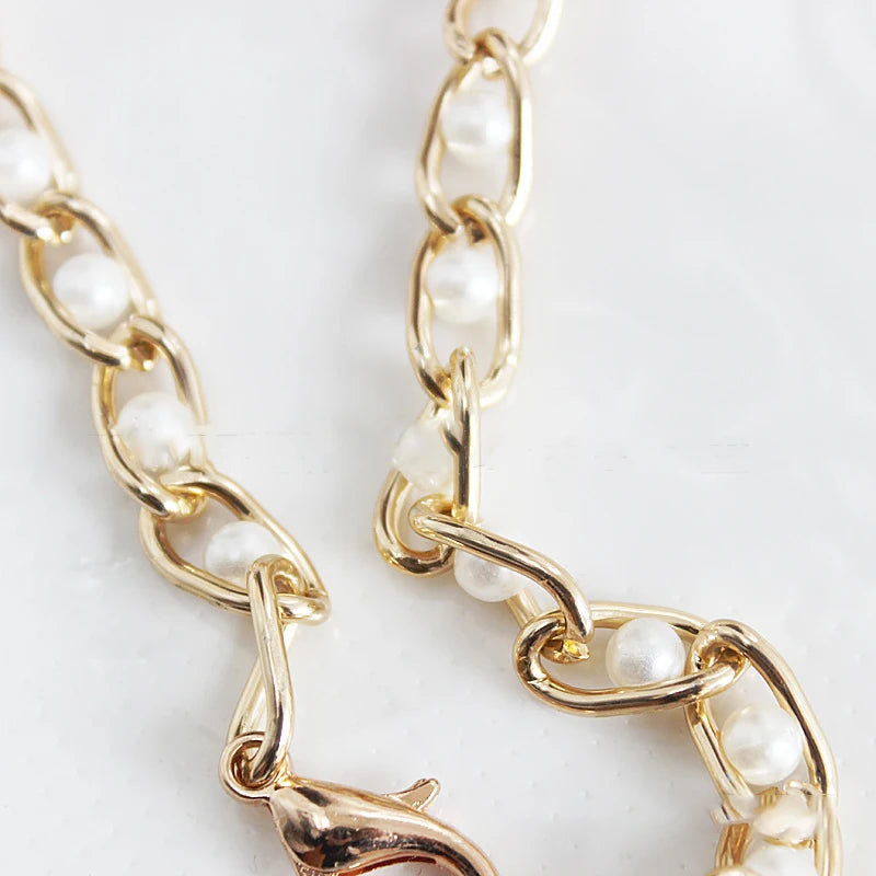 A close-up of a gold-toned chain strap made of small white pearls.