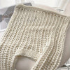 A cream-colored bohemian knit shoulder bag displayed on a white surface.