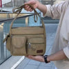 A person holds a tan canvas tool bag with multiple pockets in an outdoor setting.