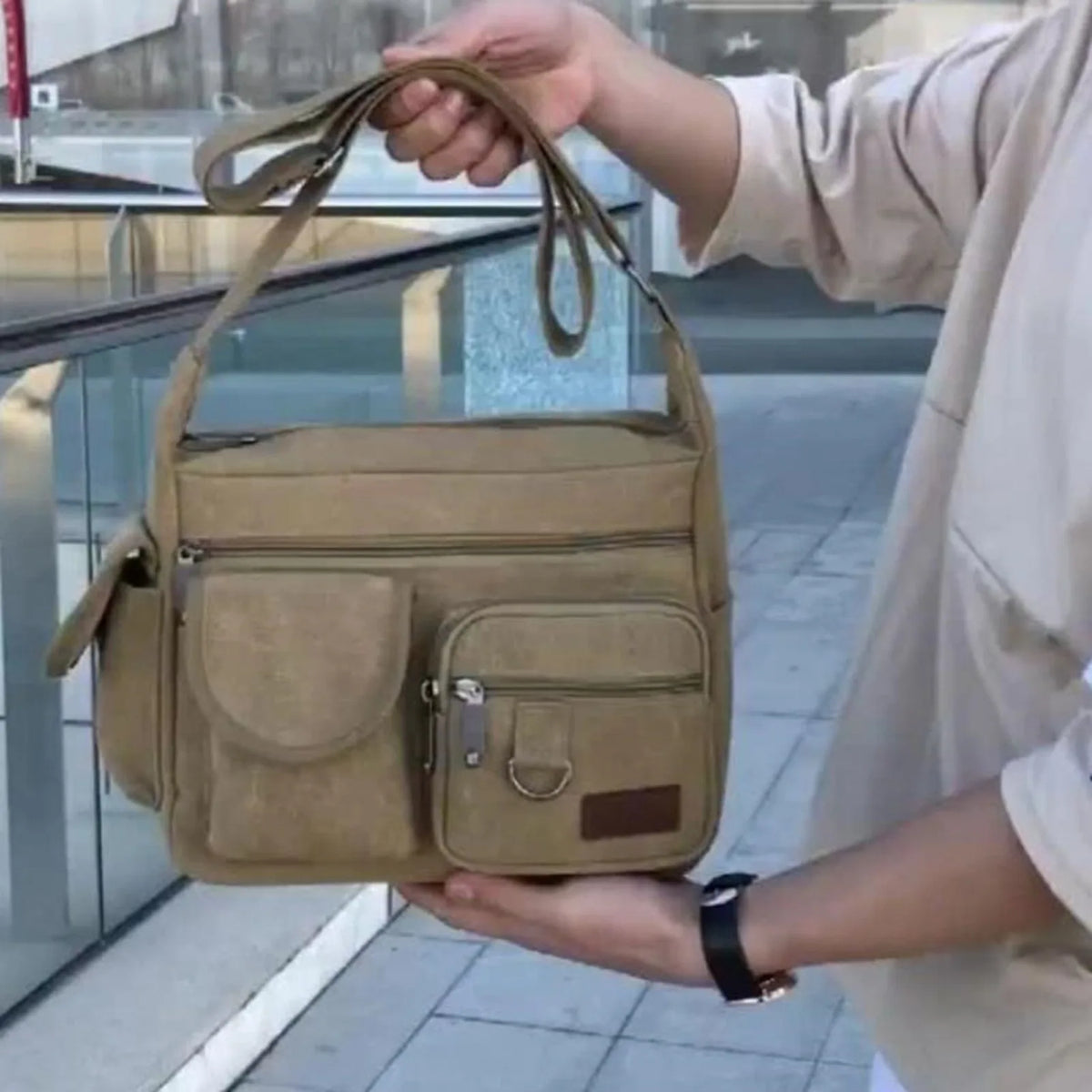 A person holds a tan canvas tool bag with multiple pockets in an outdoor setting.