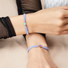 A close-up of two beaded friendship bracelets worn on a wrist, featuring light blue and purple beads.