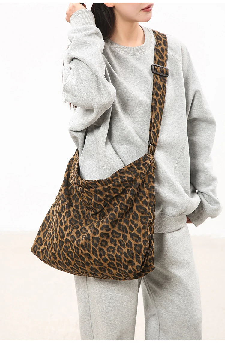 A woman is holding a brown leopard print canvas shoulder bag with an adjustable strap against a white background.