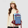 A woman wearing a beige top holds a blue and maroon lightweight travel hiking backpack.