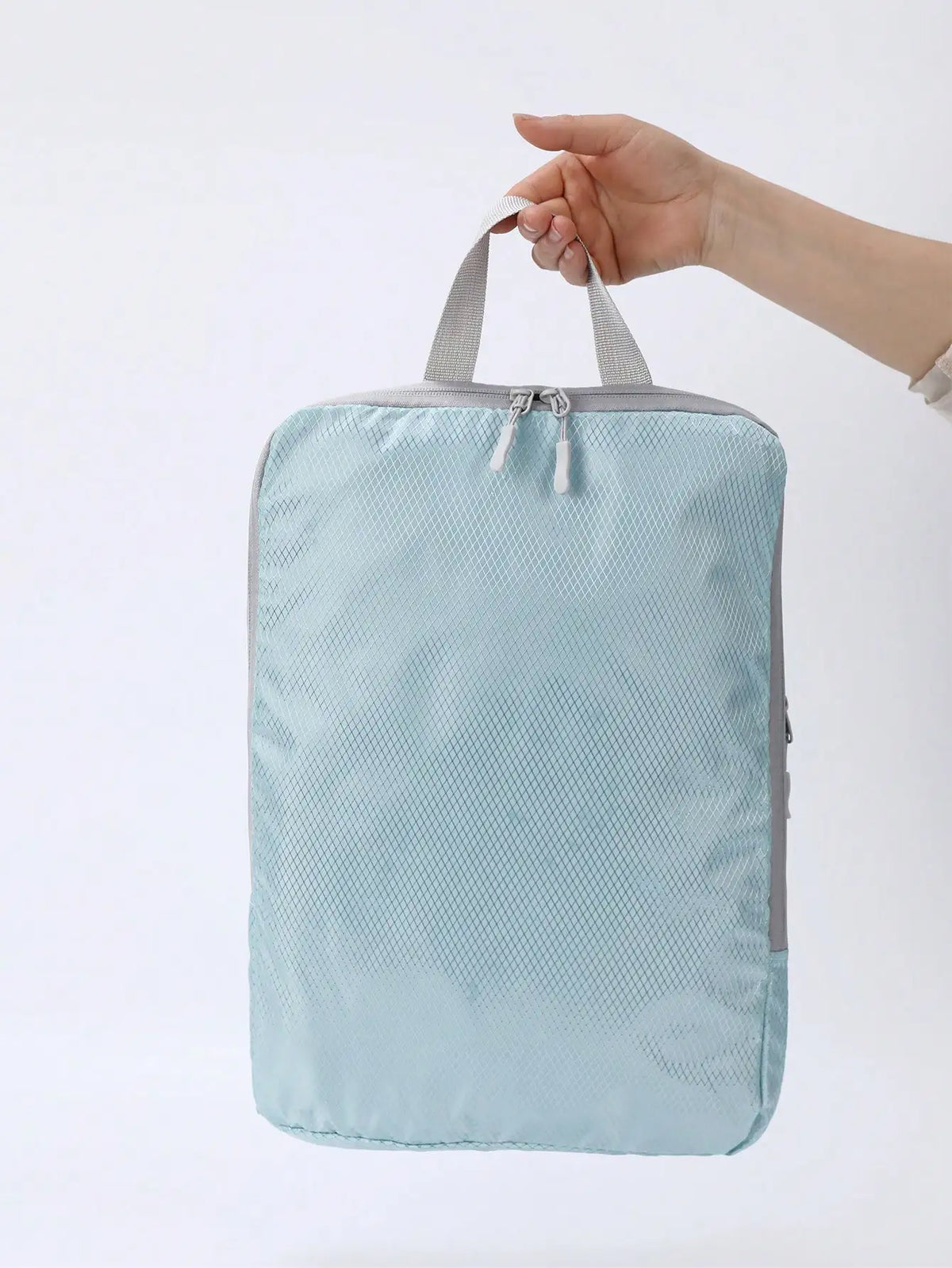 A light blue vertical travel organizer bag being held by a hand.