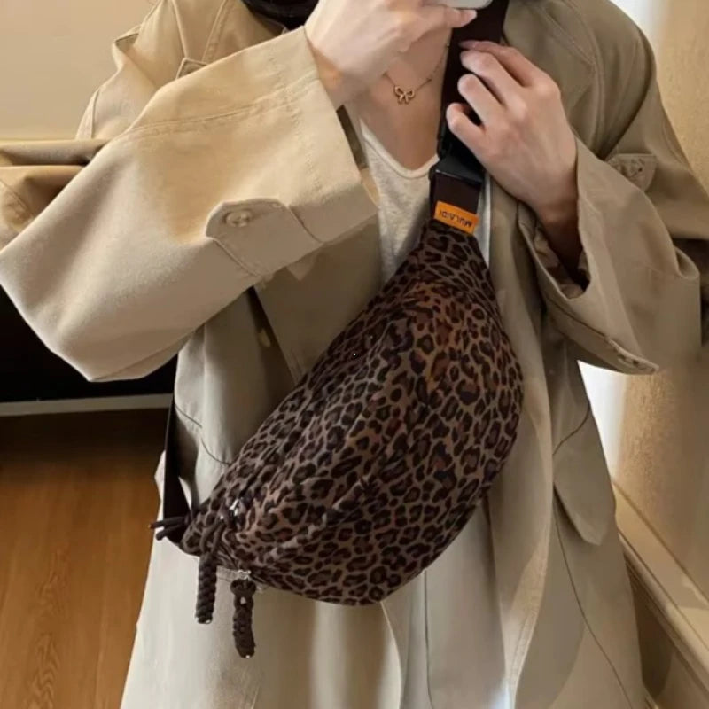 A person is holding a leopard print crossbody bag with an adjustable strap against a light beige jacket.