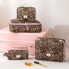 A set of leopard print travel makeup organizer bags in pink and black on a pink box.