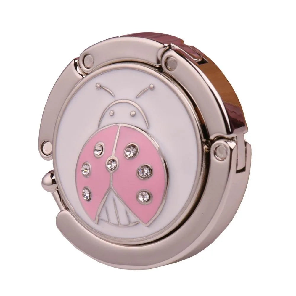 Gancho de mesa plegable de aluminio plateado con diseño de mariposa rosa.