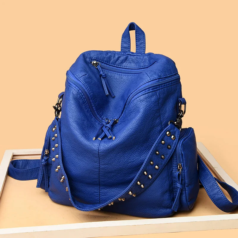 Un sac à dos en cuir souple bleu profond et rivetées, posé sur une surface en bois clair.
