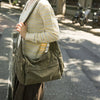 A woman wearing a cream and yellow patterned sweater carries a large olive green cotton canvas shoulder crossbody bag on a ci
